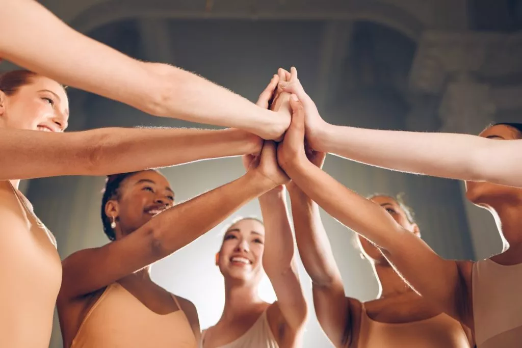 Domina los nervios en una actuación de danza. Grupo de bailarinas chocando las manos antes de una actuación de danza, dándose ánimos para calmar los nervios.