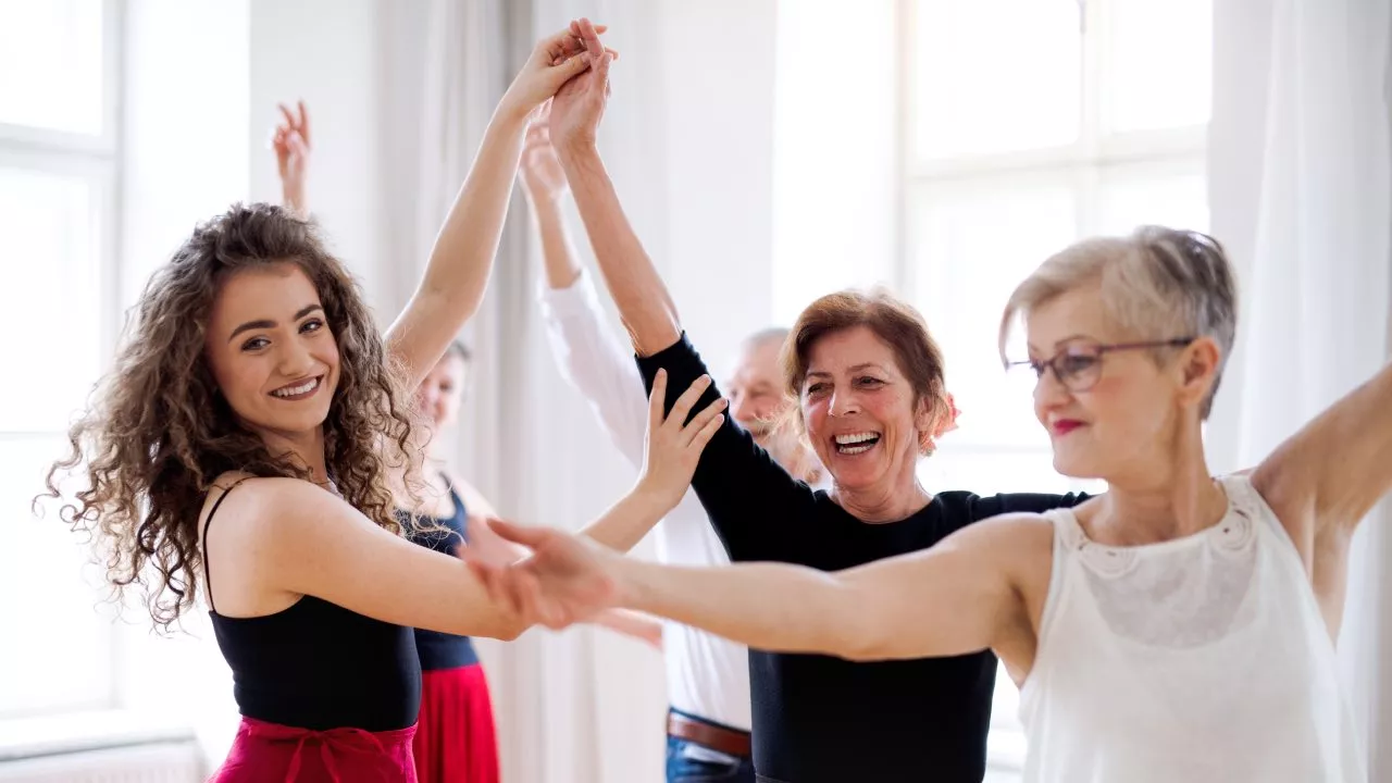 Señoras sonriendo y bailando cogidas de la mano en una clase de danza contra el Alzheimer.
